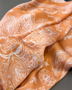 Detail of silk-satin square scarf featuring orange paisley patterns and glossy texture