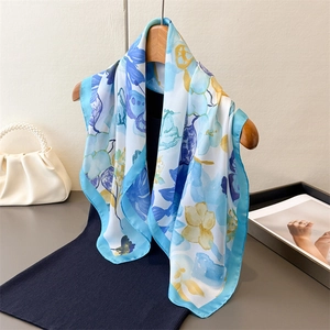 Elegant floral print silk scarf in light blue and white draped on a wooden hanger