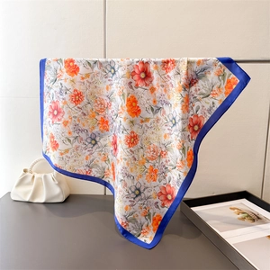 Detail of floral silk scarf with vibrant orange flowers and dark blue borders on a rack