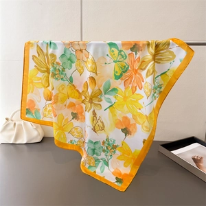 Detail of floral and butterfly print silk scarf with vibrant orange edges and satin texture