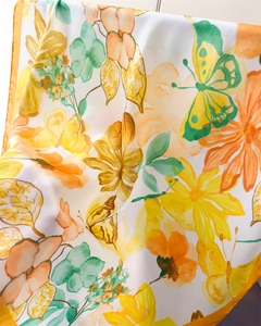 Detailed close-up of silk scarf showing vibrant floral and butterfly prints on smooth fabric