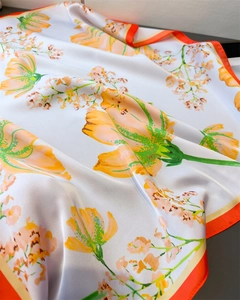 Detail of a white silk-like scarf featuring orange floral prints and stitched edges