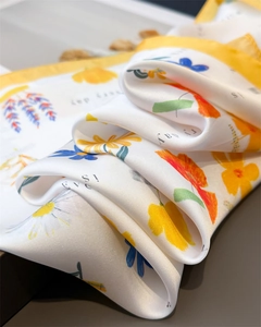 Detailed view of floral silk scarf showing vibrant daisy print and yellow hemmed edges