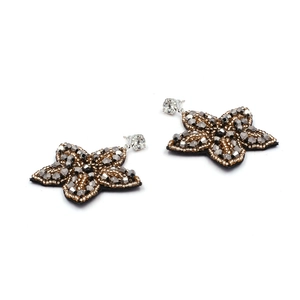 Détail de boucles d'oreilles étoiles brodées de perles dorées, argentées et noires à la main