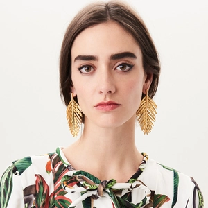 Macro detail of golden feather leaf earrings with a brushed metallic texture finish