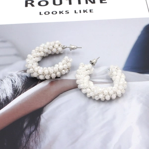 Close-up of bohemian white beaded C-shape hoop earrings on a magazine background