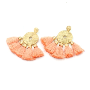 Detail of bohemian gold disc earrings with long coral peach fringe tassels on white background