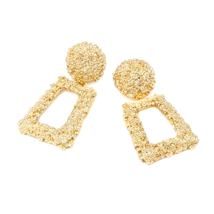 Close-up of golden geometric earrings featuring textured relief and retro floral details