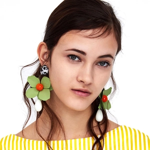 Detail of green floral earrings with orange core and white teardrop on model