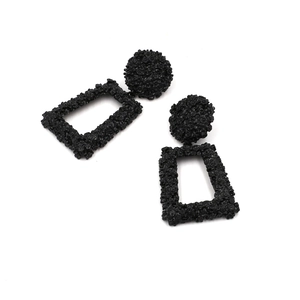 Detailed view of black geometric dangle earrings featuring textured matte floral embossing