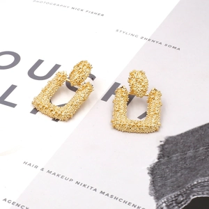 Heavy metal gold rectangular earrings with textured relief on fashion magazine background
