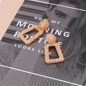Detail of geometric gold hollow earrings with granular texture on a fashion magazine