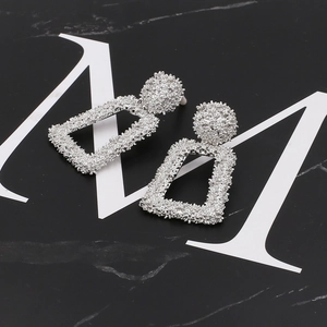 Close-up of silver textured geometric earrings with circular stud and rectangular pendant