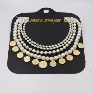 Detail of multi-layer pearl necklace with vintage gold coin pendants on a black card