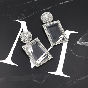 Macro detail of silver geometric earrings with clear crystals on marble background
