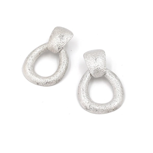 Détail de boucles d'oreilles larmes argentées avec texture métallique martelée et brossée