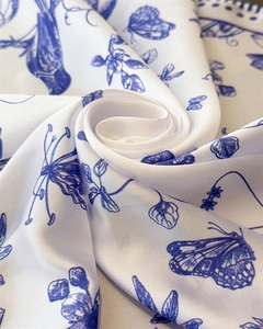 Detailed view of white faux silk scarf with blue floral butterfly print in spiral fold