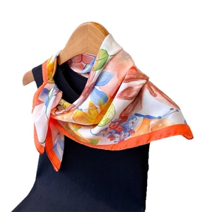 Elegant floral silk scarf with orange borders on a black top and wooden hanger