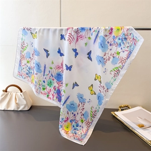 Detail of white silk scarf with blue floral prints and butterflies hanging by a handbag