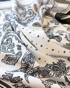 Close-up of premium silk scarf featuring black paisley and polka dot patterns with a smooth sheen