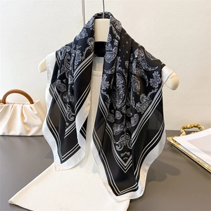 Elegant black and white paisley silk scarf displayed on a white outfit with a handbag