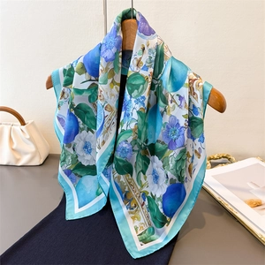 Elegant floral print silk scarf with blue flowers and green leaves on a wooden hanger