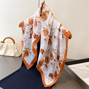 Floral satin silk square scarf with orange flower prints hanging on a wooden hanger
