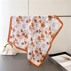 Detailed view of floral satin square scarf with orange borders draped on a metal stand
