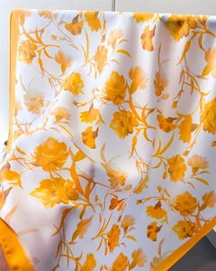 Close-up of elegant floral print on yellow satin silk square scarf with soft drape