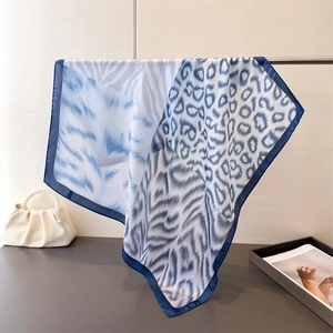 Detail of silk-like square scarf featuring blue and white animal print on metal stand