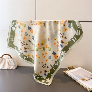 Silk-like square scarf with floral print and dark green border hanging on display