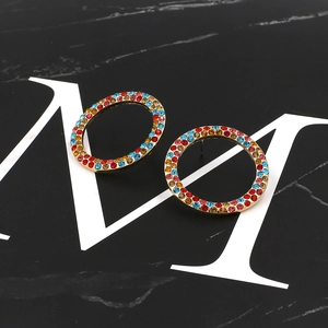 Boucles d'oreilles dorées rondes avec cristaux colorés sur fond de marbre noir