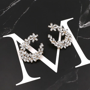 Boucles d'oreilles fleurs en C dorées avec cristaux sur une surface de marbre noir