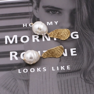 Elegant baroque pearl drop earrings with hammered gold metal plating on a fashion background