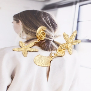 Close-up of asymmetric gold starfish and seashell earrings with matte textured finish