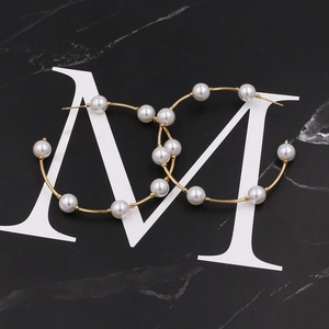 Chic oversized gold hoop earrings with white pearls on a black marble background