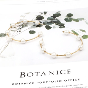 Chic gold hoop earrings with white pearls on a botanical magazine background