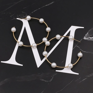 Detailed close-up of large gold hoop earrings with white pearls on a black marble base