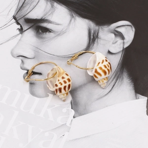 Golden hoop earrings with natural conch shell pendants on a stylish magazine background