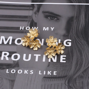 Elegant gold flower stud earrings with three clustered blossoms on a vintage magazine