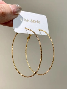 Detailed view of large golden hoop earrings with textured finish on a chic display card