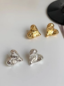 Detailaufnahme von herzförmigen Lava-Ohrringen mit goldener und silberner Hammerschlagstruktur