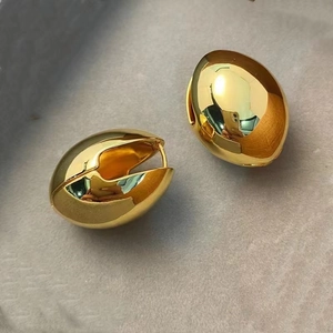 Macro detail of oval golden hinged hoop earrings with high-gloss polished metallic finish