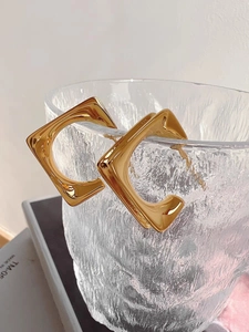 Detail of gold geometric square earrings displayed on textured glass with a warm glow
