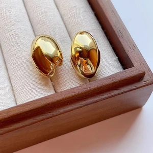Detail showing high-polished gold bean drop earrings on a white velvet jewelry holder