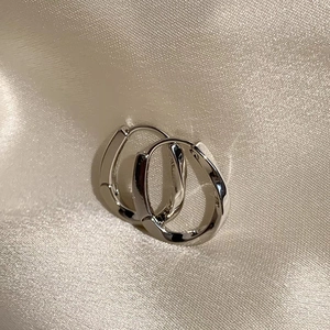 Polished silver twisted geometric hoop earrings on elegant beige silk fabric background