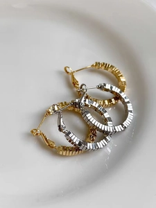 Close-up of gold and silver hoop earrings with geometric tiered texture on white tray