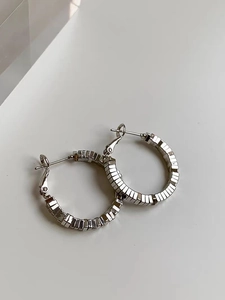 Close-up of silver geometric hoop earrings with layered rectangular textures