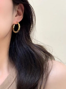 Close-up of golden round hoop earrings with geometric faceted texture on a model