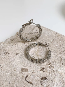 Close-up of silver geometric tiered hoop earrings on natural white textured stone